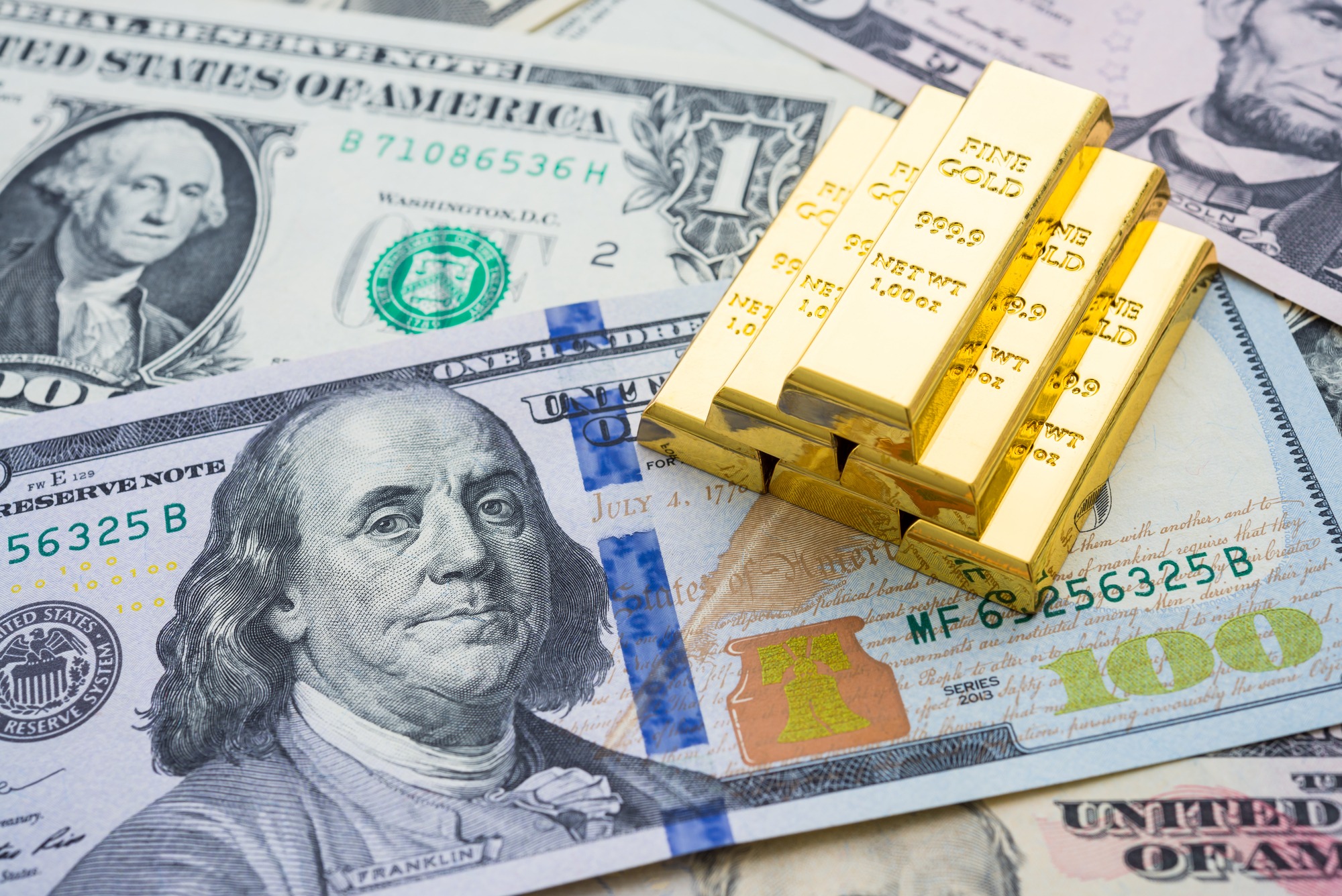 Gold bars are stacked on U.S. dollar bills, symbolizing wealth and investment. This image highlights financial assets and their role in economic discussions.